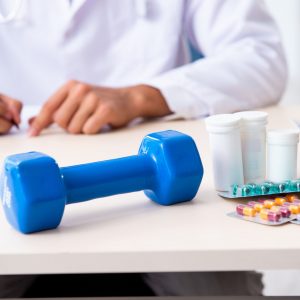 Dumbbell and pills on desk, doctor in background